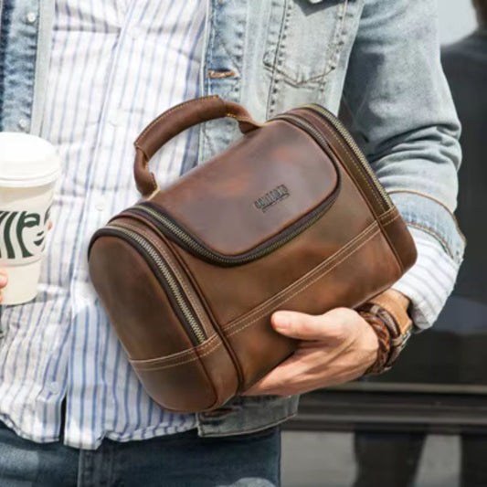 Un homme portant une veste en jean tient une Trousse de toilette homme en cuir marron et un gobelet de café.