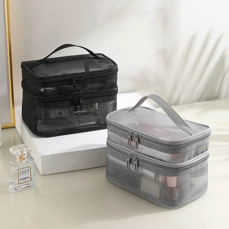 Deux trousses de toilette femmes, l'une noire et l'autre grise, sont posées sur une surface claire.
Les trousses sont de forme rectangulaire avec une poignée sur le dessus et deux compartiments zippés.
Elles sont faites d'un matériau en maille transparente permettant de voir leur contenu.
Un flacon de parfum est visible à l'arrière-plan, suggérant l'usage de ces trousses pour des produits de beauté.