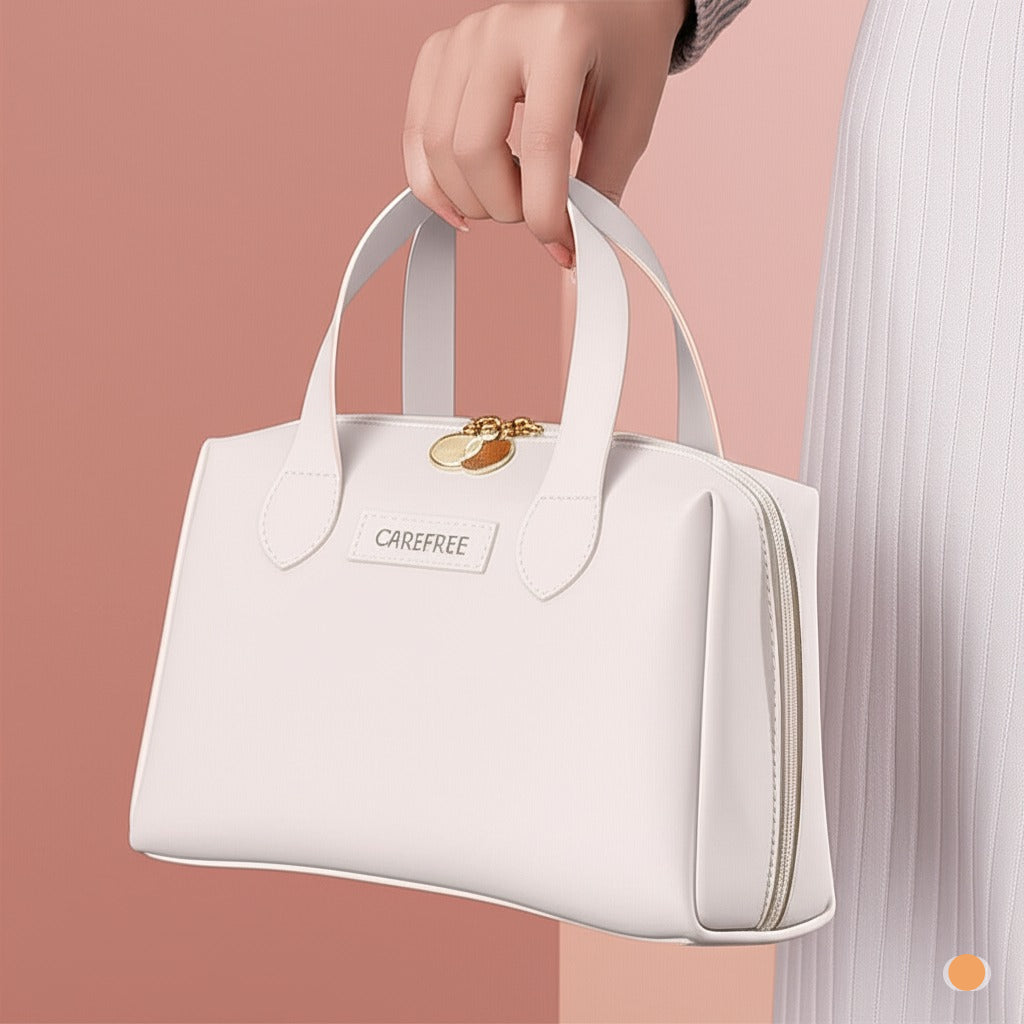 Une main féminine tient un élégant Trousse de toilette femme blanc avec des détails dorés et l'inscription "CAREFREE" sur un fond rose clair et une jupe blanche texturée est partiellement visible. Le sac a une forme structurée avec des poignées doubles et une fermeture éclair discrète sur le côté. Un petit ornement doré est attaché aux fermetures éclair du dessus.