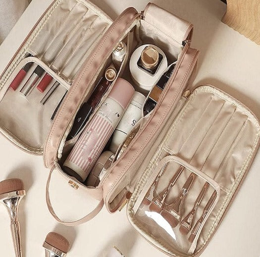 Une trousse de toilette luxe femme en cuir rose pâle, ouverte et remplie de divers cosmétiques et pinceaux de maquillage. L'intérieur beige clair contraste élégamment avec l'extérieur. Des pinceaux de maquillage supplémentaires sont disposés à côté de la trousse sur une surface claire.