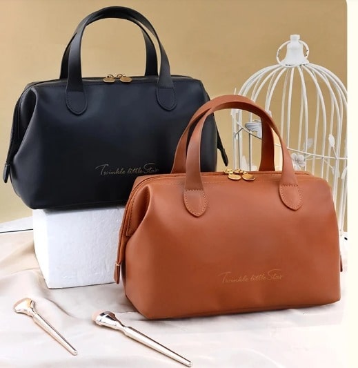 Deux élégantes Trousse de toilette femme luxe, l'une noire et l'autre marron, sont posées sur une surface claire avec des accessoires dorés à proximité. L'inscription délicate "Twinkle little star" orne le devant de chaque trousse. Un fond be