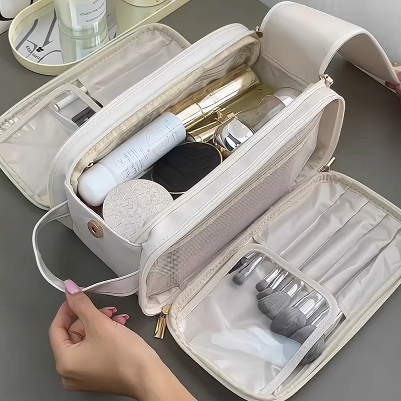 Une trousse de toilette de luxe femme, élégante et spacieuse, en cuir blanc souple avec des fermetures éclair dorées.
L'intérieur révèle plusieurs compartiments organisés, contenant divers produits de beauté et de soins personnels.
Des pinceaux de maquillage sont rangés dans des pochettes dédiées, tandis que des flacons et des pots sont disposés dans les sections principales.
Un accessoire de voyage idéal, alliant fonctionnalité et sophistication pour la femme moderne.