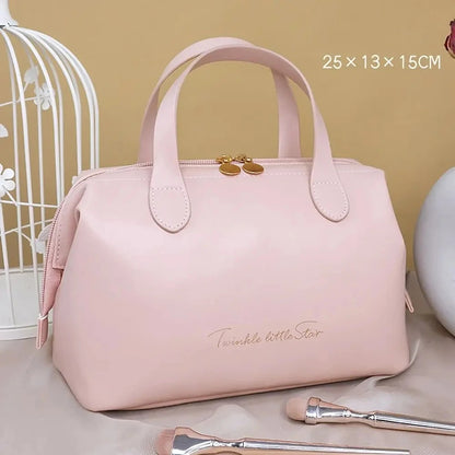 Élégante Trousse de toilette femme luxe Rose en cuir synthétique, de forme rectangulaire avec des coins arrondis et deux anses sur le dessus. Une fermeture éclair dorée sécurise le contenu. L'inscription délicate "Twinkle little Star" orne la face avant en lettres cursives dorées. La trousse est posée sur un tissu satiné beige, avec un coin de cage décorative blanche visible à gauche et des pinceaux de maquillage au premier plan.