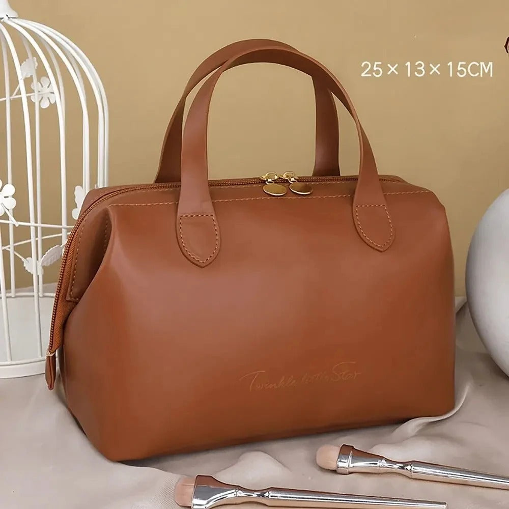 Élégante Trousse de toilette femme luxe marron en cuir synthétique, de forme rectangulaire avec des coins arrondis et deux anses sur le dessus. Une fermeture éclair dorée sécurise le contenu. L'inscription délicate "Twinkle little Star" orne la face avant en lettres cursives dorées. La trousse est posée sur un tissu satiné beige, avec un coin de cage décorative blanche visible à gauche et des pinceaux de maquillage au premier plan.