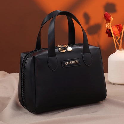 Trousse de toilette femme" sur une étiquette apposée sur une élégante trousse de toilette Noir, de forme structurée avec des anses, posée sur un tissu clair et froissé, avec un fond brun et un vase blanche contenant des fleurs séchées rouges. Le nom de la trousse sera "Carefree".