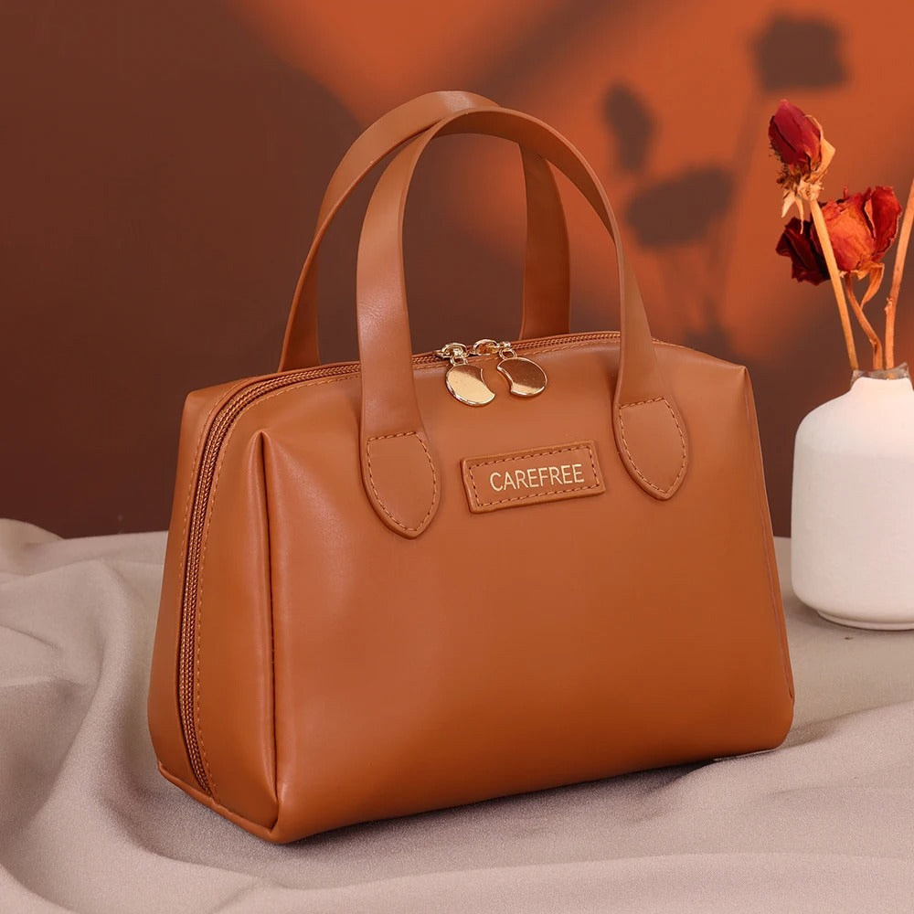 Trousse de toilette femme" sur une étiquette apposée sur une élégante trousse de toilette marron, de forme structurée avec des anses, posée sur un tissu clair et froissé, avec un fond brun et un vase blanche contenant des fleurs séchées rouges. Le nom de la trousse sera "Carefree".